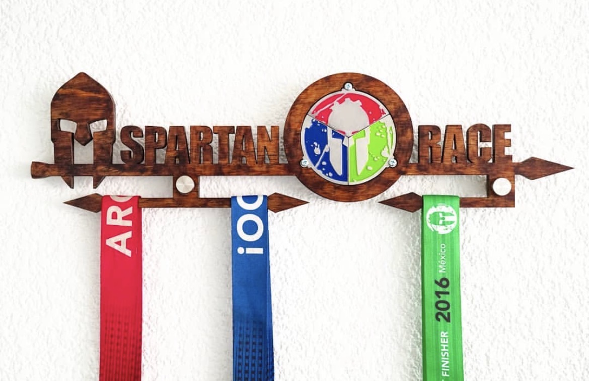 Porta medallas de madera cortado a láser con la leyenda Spartan Race y medallas colgando