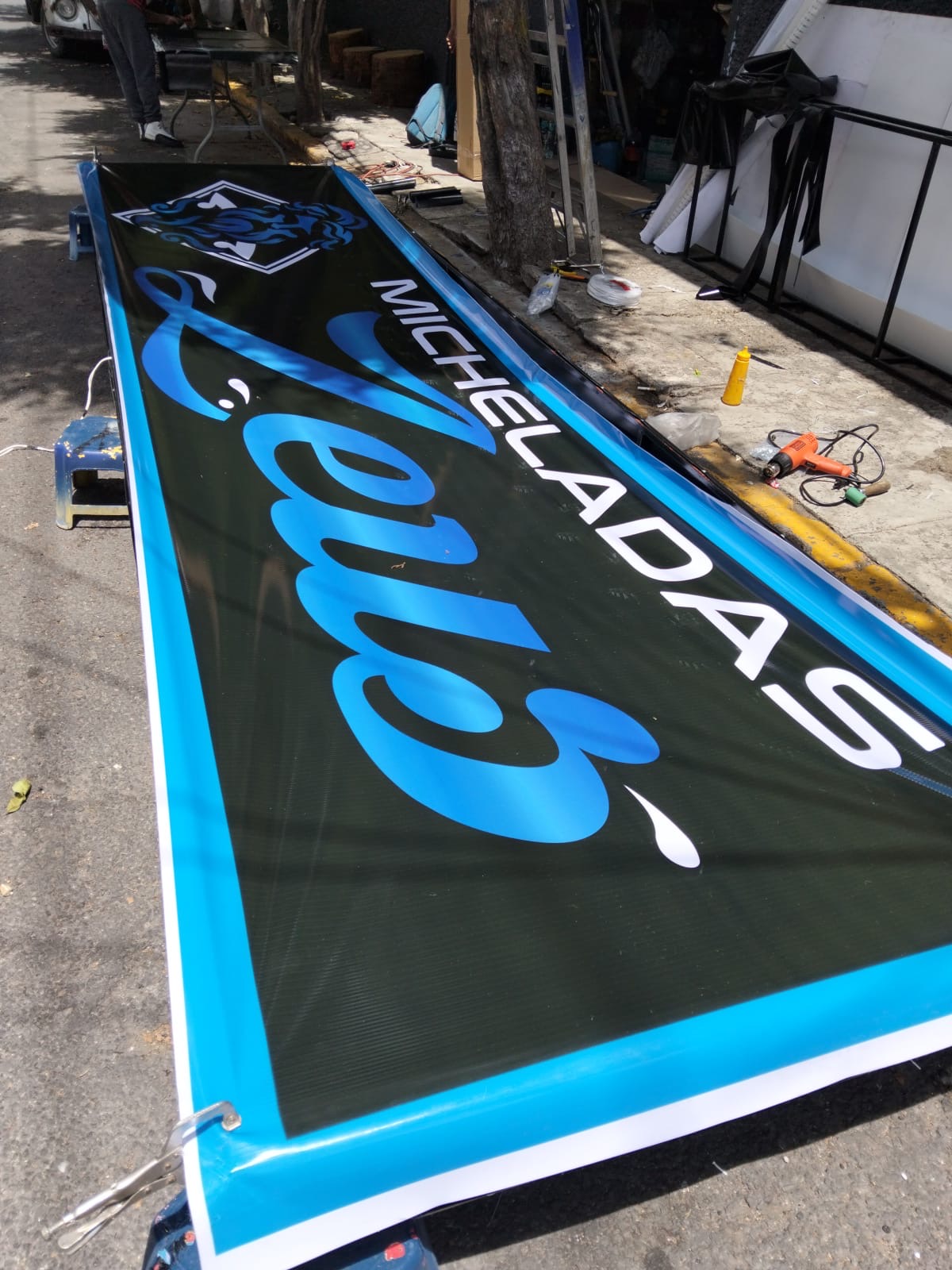 Panel publicitario negro con diseño azul terminado en el exterior del taller