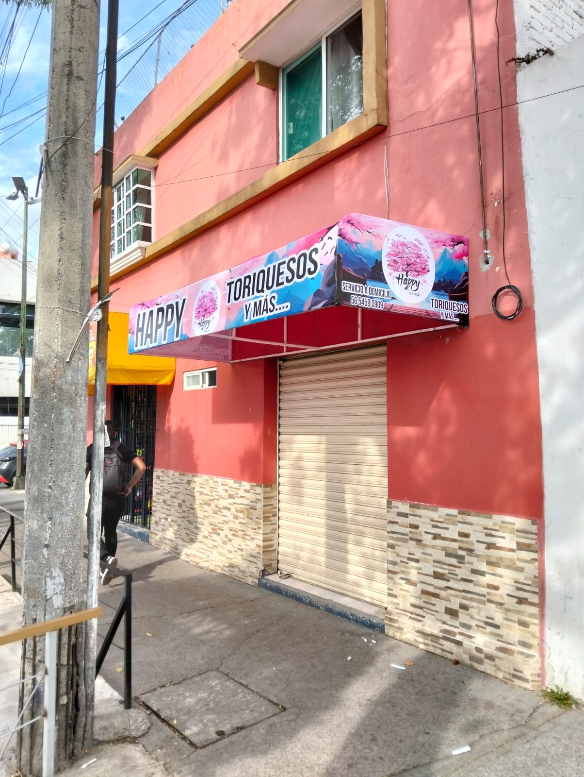 Toldo impreso instalado sobre la entrada de un local de comida con fachada rosa