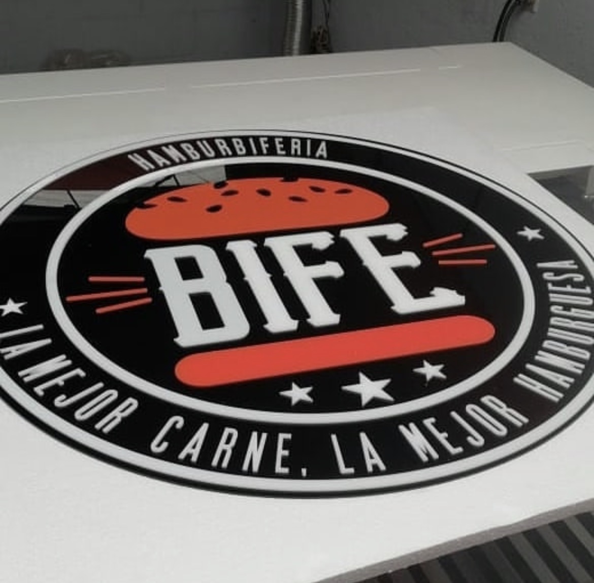 Emblema circular de acrílico negro, blanco y rojo con el logotipo BIFE